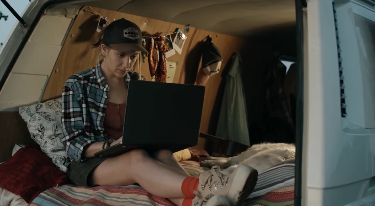 Woman in casual clothes using a laptop inside a cozy, well-decorated van.