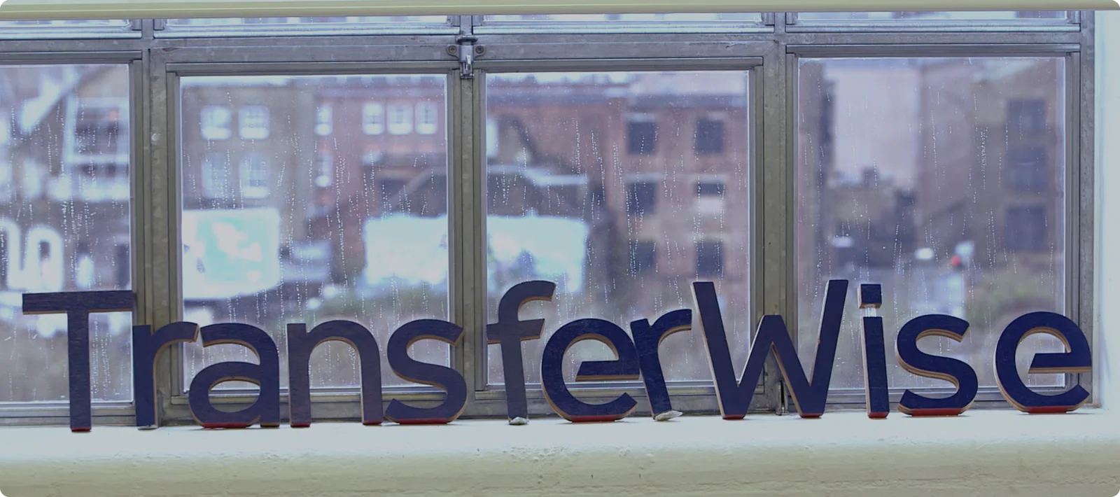 Blue TransferWise logo displayed near a window with a blurred urban background.