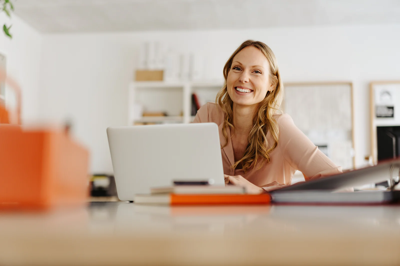 Happy sincere young businesswoman with a warm friendly smile Happy sincere young businesswoman with a warm friendly smile and laughing eyes looking at the camera around the side of her laptop in a low angle view with copyspace